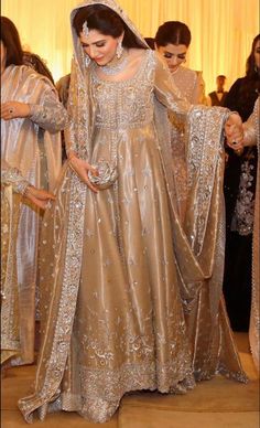 a woman in a wedding dress and veil walking down the aisle with other people behind her