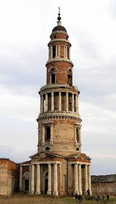 an old tower with people walking around it in the middle of a grassy area next to some buildings