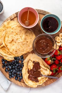 a plate with pancakes, fruit, and chocolate sauce on it next to two cups of coffee