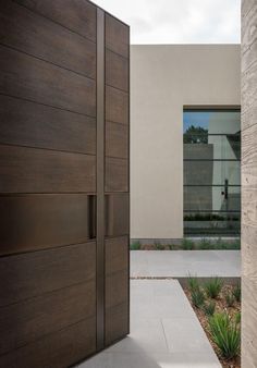 an entrance to a modern home with wood doors and stone walkway leading up to the front door