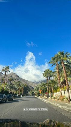 cars are driving down the street in front of palm trees and mountain range on a sunny day