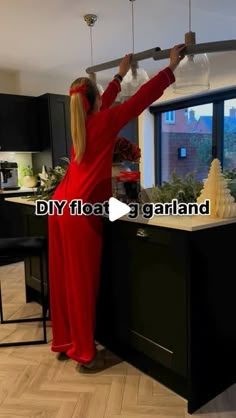 a woman in a red jumpsuit is standing at the kitchen counter and reaching for something