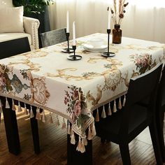 a dining room table covered with a white table cloth and two candles on it, in front of a couch