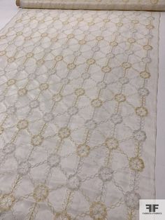 a white rug with gold and silver designs on the floor next to a roll of fabric