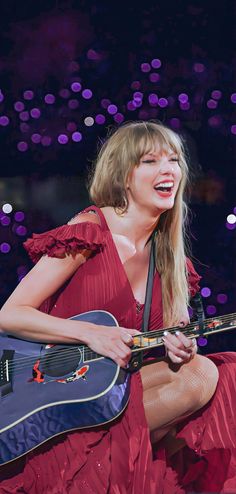 a woman in a red dress holding a guitar and singing into the microphone with her mouth open