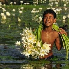 a young boy is holding flowers in the water with his arms wrapped around him and smiling at the camera