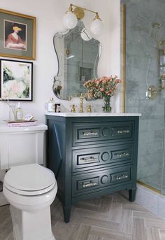 a white toilet sitting next to a bathroom sink under a vanity with flowers on it