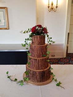 a tall wooden cake with flowers on top and greenery in the middle, sitting on a table