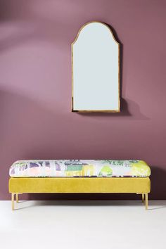 a yellow bench with a mirror on the wall above it and a pink wall behind it