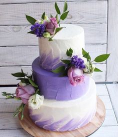 a three tiered cake with purple and white frosting, flowers on each layer