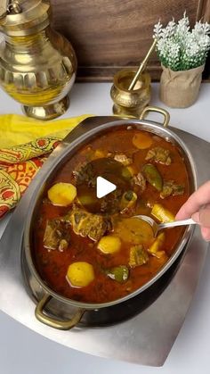 a person holding a spoon over a pot of stew on a table with other items