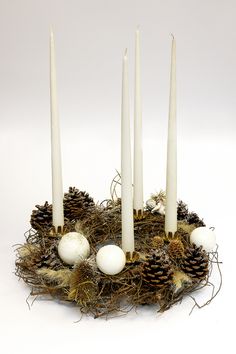 four white candles sitting on top of a nest with pine cones and balls around it