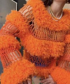 a woman in an orange fuzzy dress with pearls on her head and hands behind her back