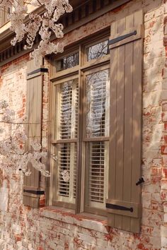 an old brick building with shutters and flowers in the window sill on either side