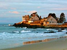 houses on an island in the ocean with waves coming up to them and blue sky above