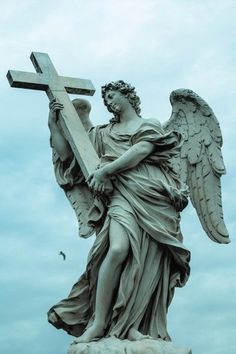 an angel holding a cross on top of a statue