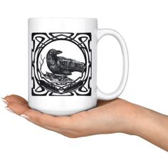 a hand holding a white coffee mug with a black bird on it