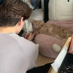 a man laying on the floor next to a cat sleeping in a bed with his head on a pillow