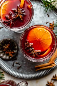 two glasses filled with red wine and an orange slice on top of a metal tray