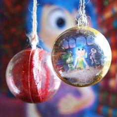 two christmas ornaments hanging from strings in front of a cartoon character