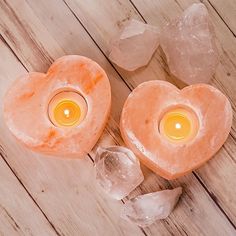 two heart shaped candles sitting next to ice crystals on top of a wooden table with one candle lit in the shape of a heart