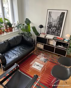 a living room with black leather couches and potted plants in the corner,