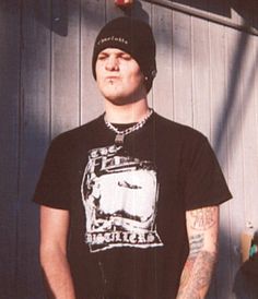 a man standing in front of a building wearing a black shirt and beanie hat