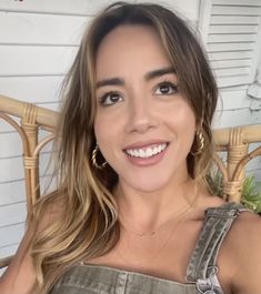 a woman sitting in a chair with her eyes closed and wearing gold hoop earrings, smiling at the camera