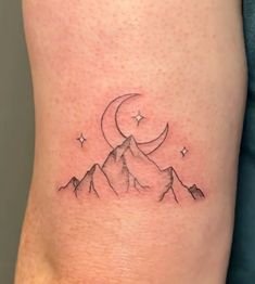 a small tattoo on the leg of a woman with mountains and stars in the sky