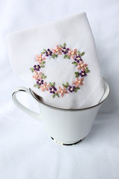 a white cup with a napkin on top of it and a flower embroidered on the side