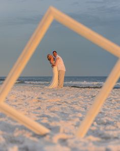 a bride and groom standing on the beach in front of an empty square photo frame