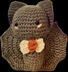 a crocheted teddy bear with a bow tie on it's chest, sitting in front of a black background