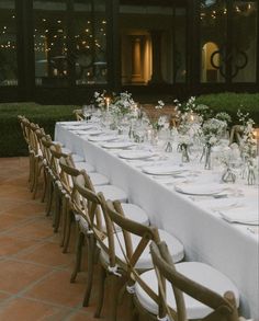 a long table is set up with white linens and place settings for dinner guests