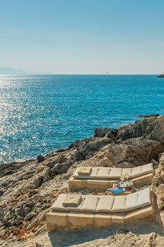 two lounge chairs sitting on top of a sandy beach next to the ocean