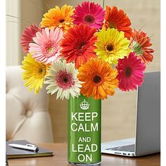 a vase filled with colorful flowers sitting on top of a table next to a laptop