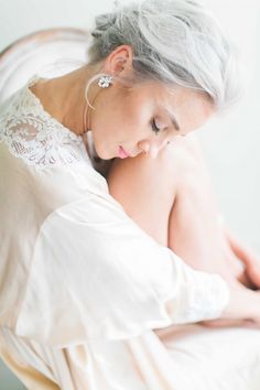 an older woman with grey hair wearing a white dress and holding her hands on her chest