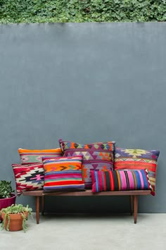 a couch sitting next to a cement wall covered in colorful pillows and potted plants