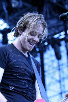 a young man playing an electric guitar at a music festival in front of a microphone