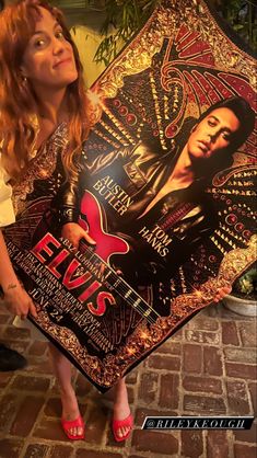 a woman holding up a scarf with elvis presley on it and red guitar in the background