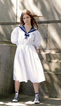 a woman in a sailor's dress leaning against a wall with her hair blowing in the wind