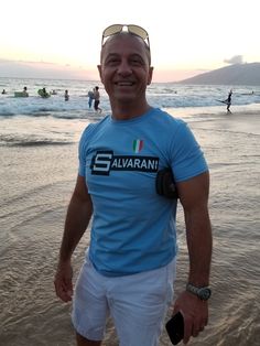 a man standing on top of a sandy beach next to the ocean with people in the background