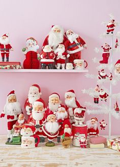 santa clause figurines and other christmas decorations on shelves in a pink walled room