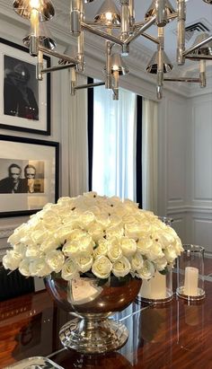 a vase filled with white roses on top of a wooden table in front of a mirror