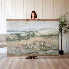 a woman holding up a large painting in front of her face and smiling at the camera