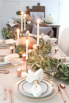 a dining room table with candles, plates and greenery on it's centerpiece