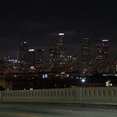 the city skyline is lit up at night from an overpass with cars driving on it