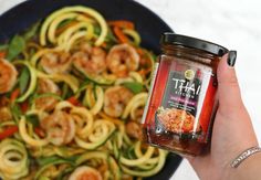 a hand holding a jar of pasta sauce next to a bowl of zucchini noodles