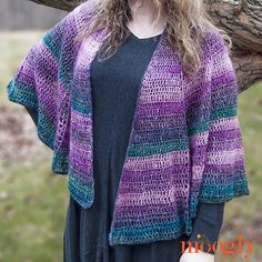 a woman standing next to a tree wearing a purple and green knitted cardigan