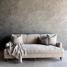 a couch with several pillows on it in front of a gray wall and concrete floor