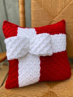 a red and white crocheted pillow with a bow on it's side